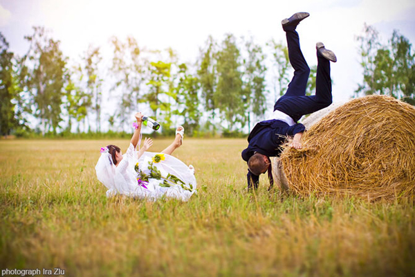 Bride and groom tumbling near a hay bale in a field
