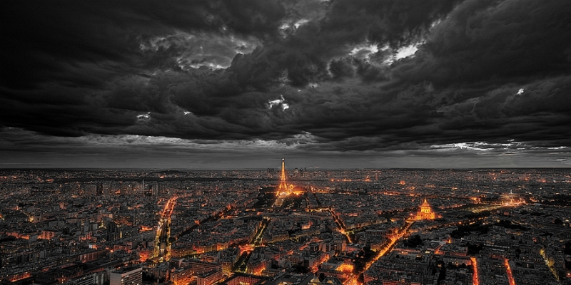 Moody aerial of the glowing Eiffel Tower under a dark stormy night sky