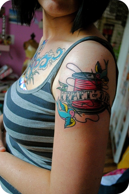 Neo-traditional shoulder tattoo of a red spool with banner reading Craft or Die