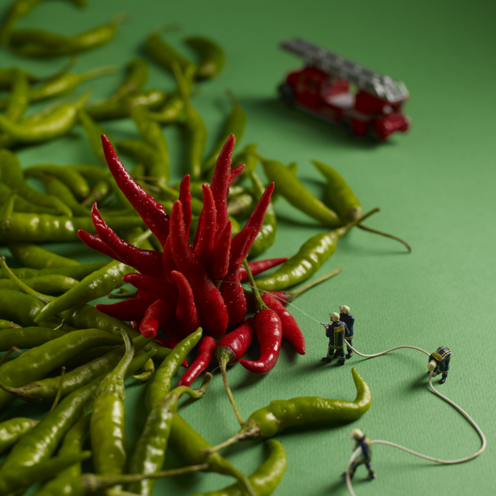Miniature firefighters aiming a hose at red chili peppers