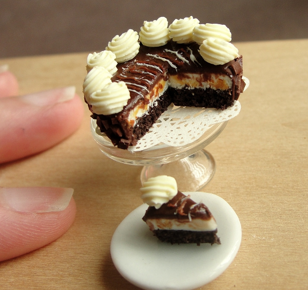 Miniature layered chocolate cake on a glass stand with a plated slice