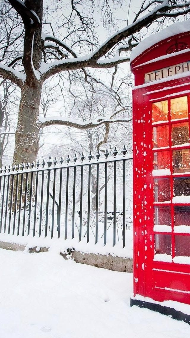 Snow-dusted red telephone box glowing beside a park fence