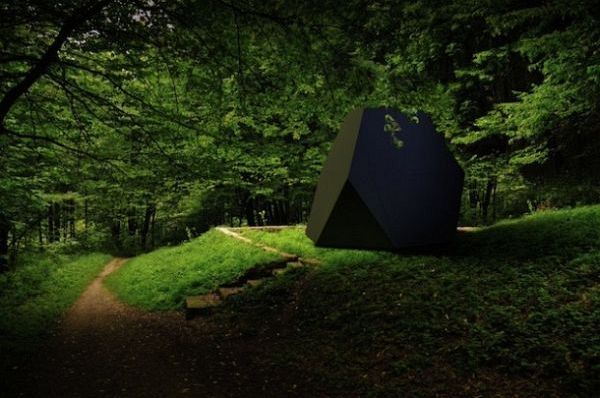 Closed black tetrahedral office shed among trees