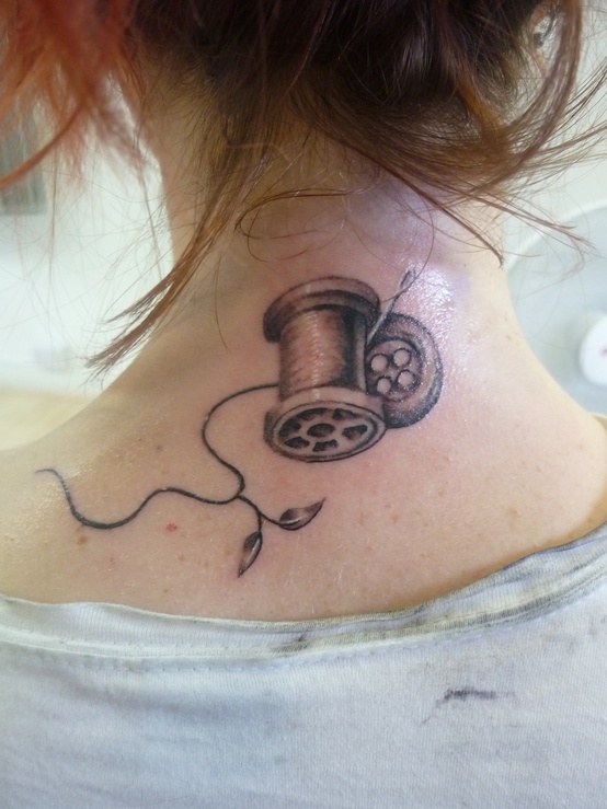 Black-and-grey nape tattoo of a spool, button, and needle with a trailing thread