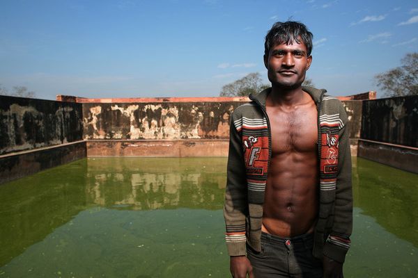 awesome-india-photos01 Man in open striped hoodie before a green water tank