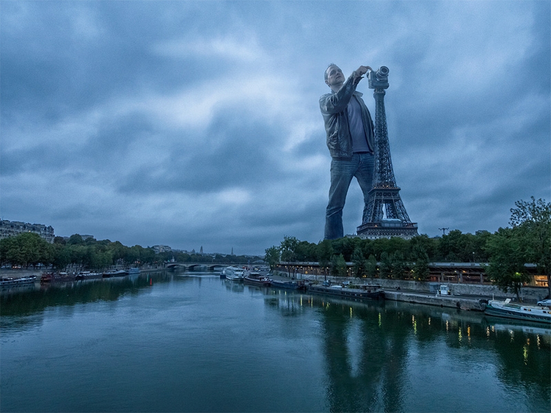 Surreal composite of a giant photographer using the Eiffel Tower as a tripod