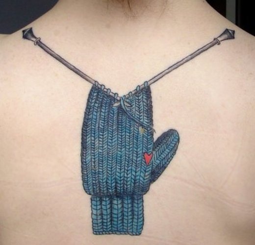 Upper-back tattoo of a blue knitted mitten still on the needles