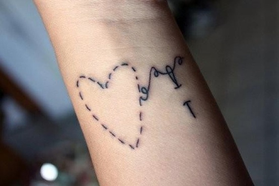 Wrist tattoo of a heart outlined in dashed stitch marks with a needle