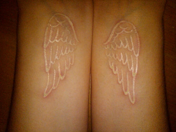 Paired white ink angel wing tattoos on inner wrists