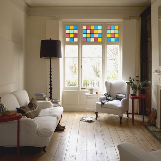 Airy living room with white seating, wood floors, and colorful window glass