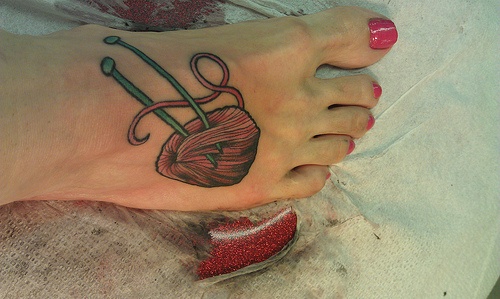 Foot tattoo of a pink yarn ball with green knitting needles