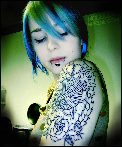 Shoulder tattoo of a yarn ball, stitch-marked heart, and roses in bold linework