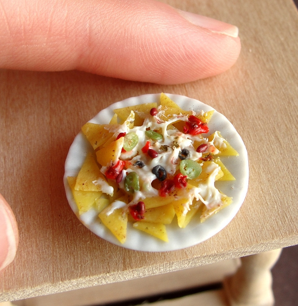 Miniature nachos with cheese, jalapeños, and olives on a scalloped plate