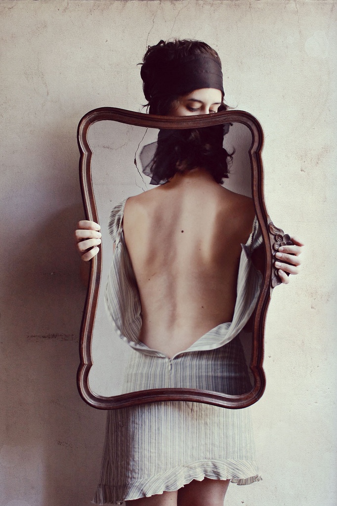 Woman holding a wavy wooden frame that reveals her bare back instead of a front reflection