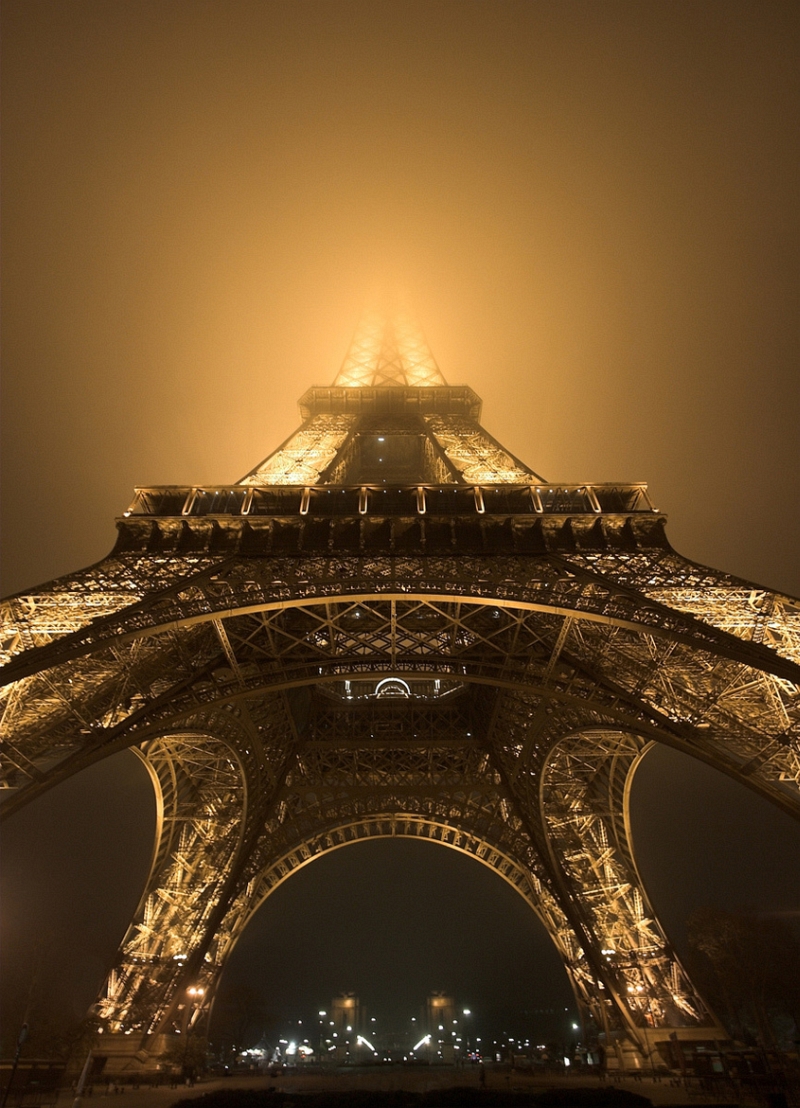 Night view upward into fog glowing around the lit Eiffel Tower base